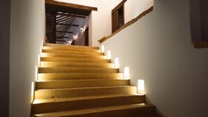 Uma escadaria com degraus iluminados que leva a um quarto com teto de madeira e uma janela.