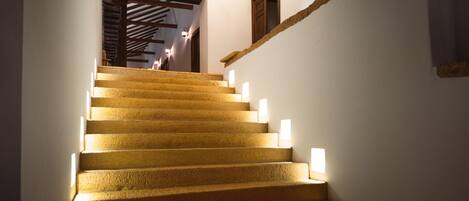 A staircase with illuminated steps leading to a room with a wooden ceiling and a window.