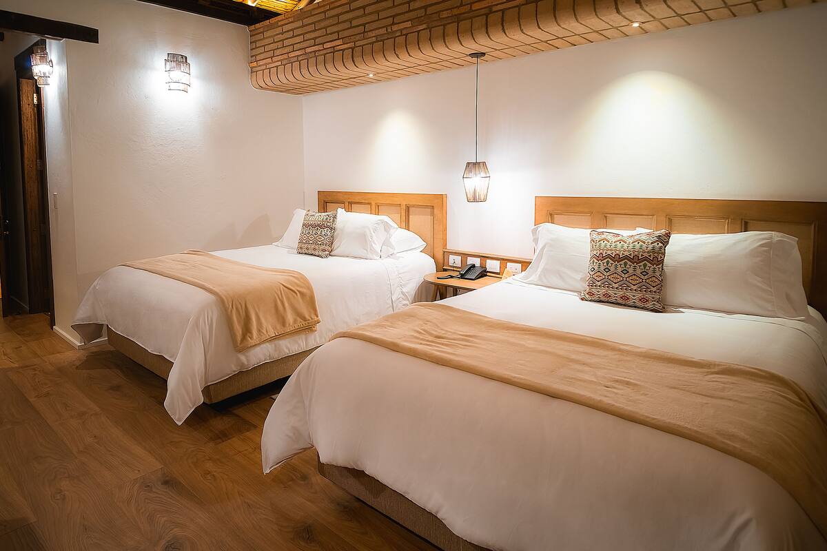 Two double beds with wooden headboards, a wooden floor, and a brick ceiling.