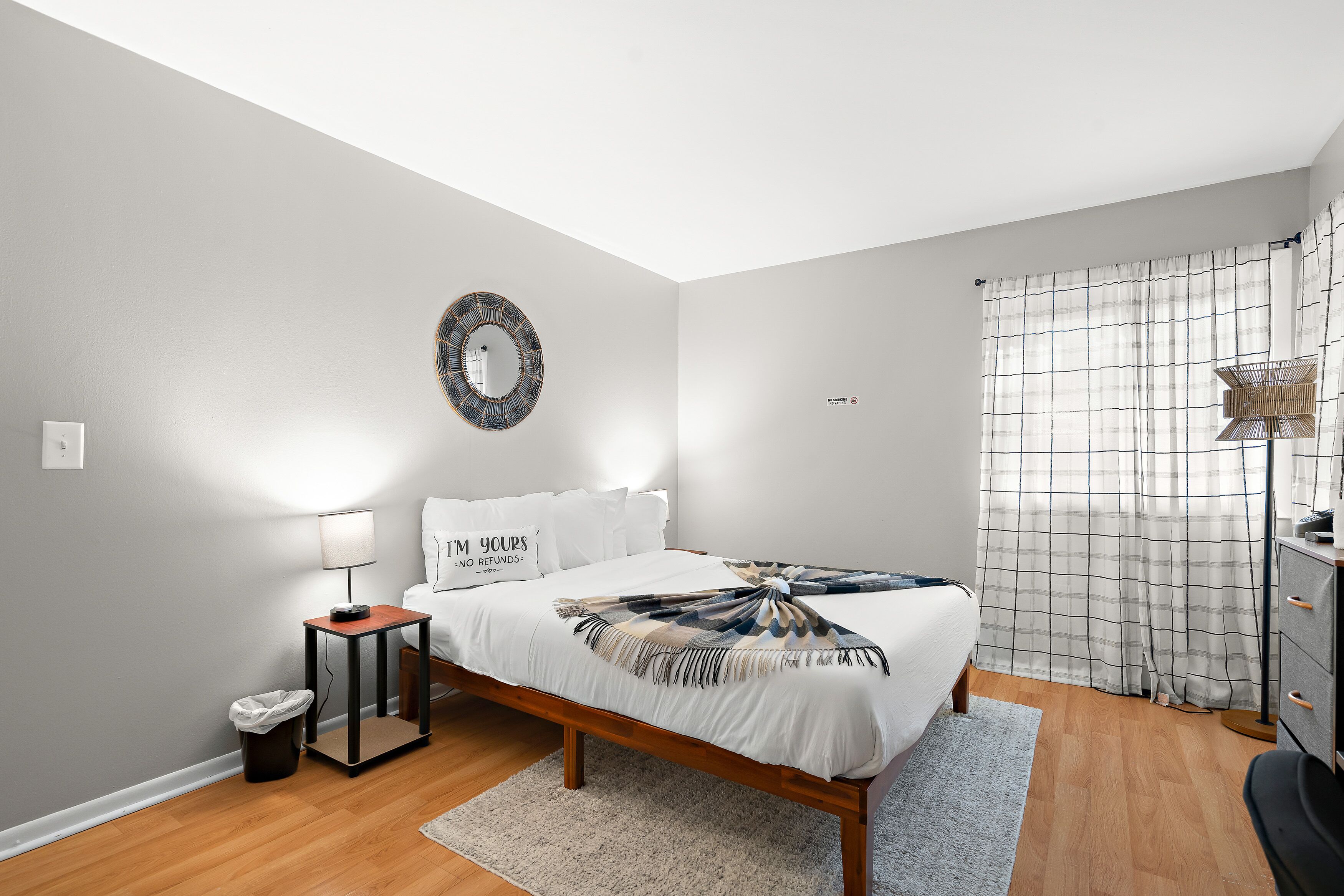 A bedroom with a bed, bedside lamp, wall-mounted mirror, and a rug.