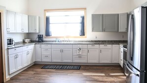 A kitchen with white cabinets, a stainless steel refrigerator, and a window with curtains. - Private, quiet & beautiful second story with peek a boo water views (Milbridge)