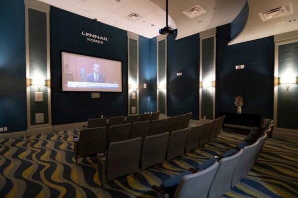 Une salle de conférence dotée d’un grand écran diffusant une présentation, de rangées de chaises et d’un tapis à motifs.
