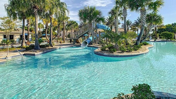 Un espace piscine aménagé dans un complexe hôtelier, avec une eau cristalline, des palmiers et un toboggan aquatique.