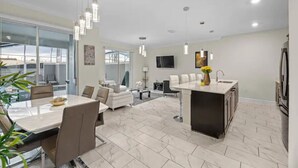 Une cuisine moderne dotée d’un îlot central, un coin repas avec une grande table et des chaises, et un espace de vie comprenant un canapé et une table basse.