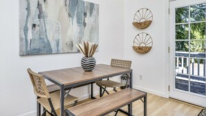A dining area with a wooden table and chairs, a large abstract painting, and two woven baskets on the wall. - Modern Home in downtown Middletown! Walk to shops & restaurants! (Middletown)