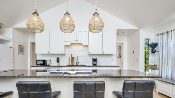 A modern kitchen with white cabinets, a central island with bar stools, and hanging wicker pendant lights. - Modern Home in downtown Middletown! Walk to shops & restaurants! (Middletown)