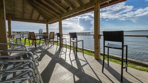 A covered outdoor seating area with chairs and tables overlooking a body of water. - Welcome to Paradise! (Navarre)