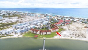 An aerial view of a coastal residential area with multiple buildings, a pier extending into the water, and a beach in the background. - Welcome to Paradise! (Navarre)
