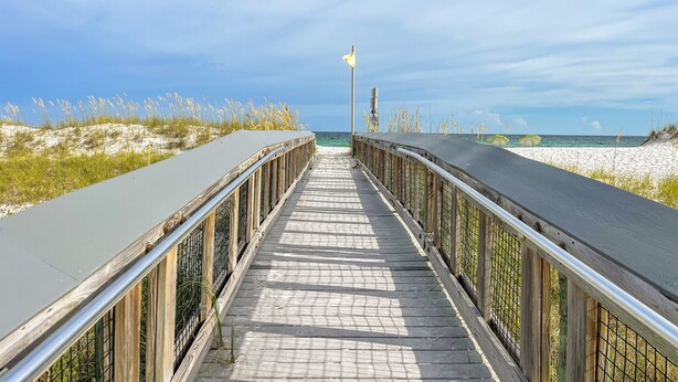 A wooden boardwalk leading to the beach with a metal railing and a flag. - Welcome to Paradise! (Navarre)