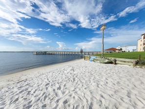 A beach with a wooden pier extending into the water, a lifeguard tower, and a building with a red roof in the background.