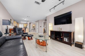 A modern living room with a leather sofa, glass coffee table, and a flat-screen TV mounted on the wall.