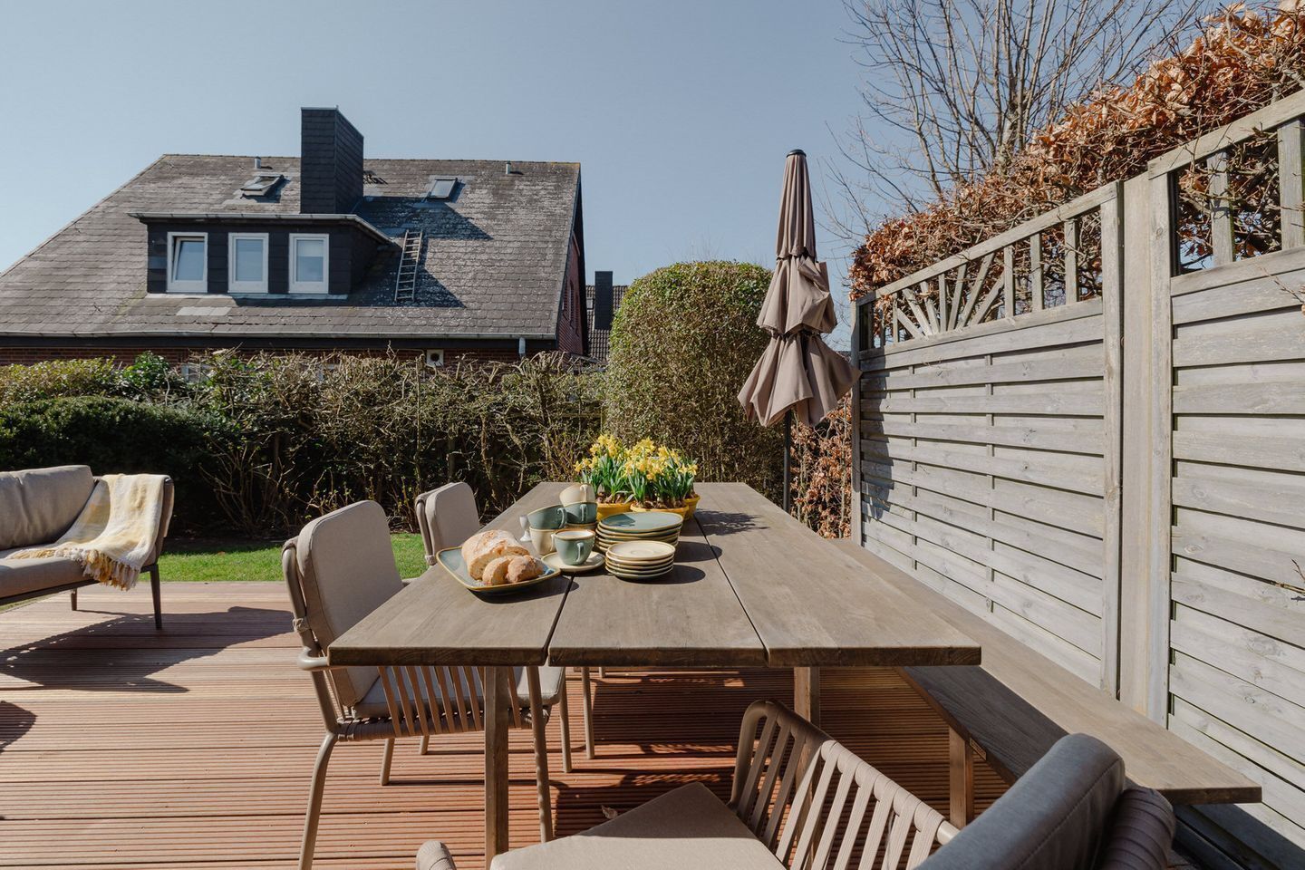 Eine Terrasse im Freien mit einem Holztisch, gedeckt für das Essen, umgeben von Stühlen.