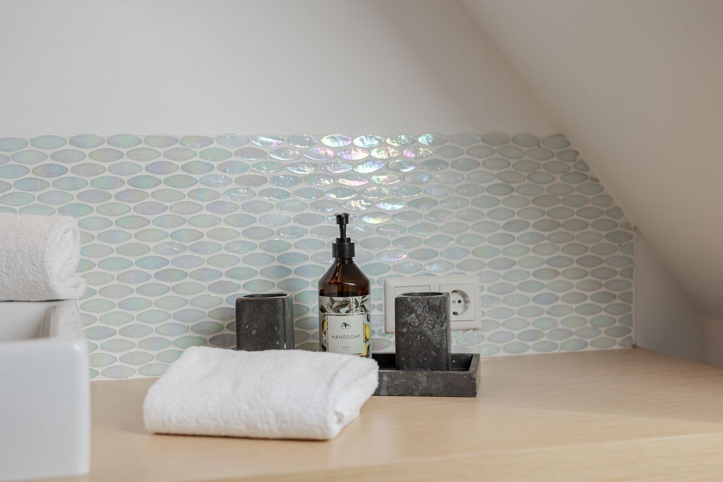 Een badkamer met een witte handdoek, een handzeepfles en een zeepdispenser op een houten blad.