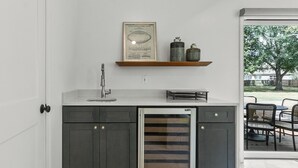 A kitchen with dark cabinets, a stainless steel sink, a built-in refrigerator, and a window overlooking a patio with outdoor furniture.