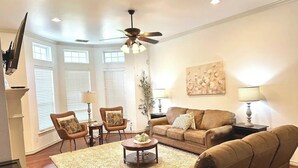 A living room with a brown leather sofa, two armchairs, a coffee table, and a ceiling fan. - 10th St Manor + Walk to Stadium + Hot Tub + Game Garage + Sleeps 20 (Lubbock)