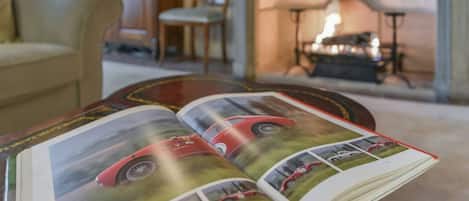 Un libro abierto con un coche rojo en la portada, sobre una mesa de madera en una habitación con chimenea.
