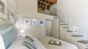 A bedroom with a bed, a bedside table, a lamp, a tray with breakfast items, a staircase, and framed pictures on the wall. - Pontormo large apartment with fireplace in Oltrarno (Firenze)