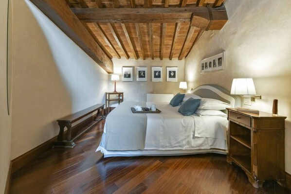 A bedroom with a wooden ceiling, a large bed with pillows, bedside tables, and framed pictures on the wall.