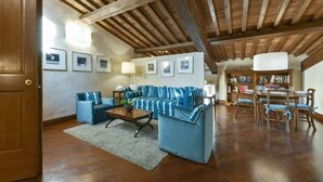 A spacious living room with a wooden ceiling, a blue-striped sofa set, a dining table with chairs, and a bookshelf. - Tiepolo romantic penthouse in the Oltrarno (Firenze)