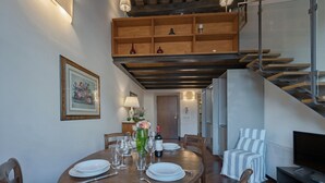 Un comedor con una mesa de madera dispuesta para cuatro personas, un televisor y una escalera que lleva a un nivel superior.