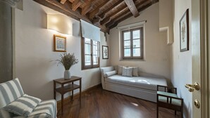 A cozy room with a wooden ceiling, a sofa, a chair, a small table with a vase, and two windows. - Tiziano big penthouse in the Oltrarno (Firenze)