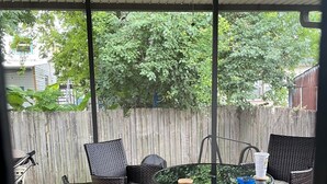 A covered patio with wicker furniture, a glass table, and a ceiling fan.