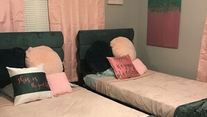 Two single beds with green headboards, pink and white bedding, and decorative pillows with text.