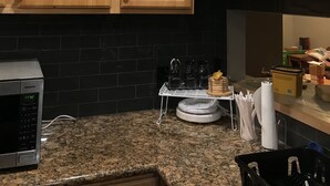 A kitchen with wooden cabinets, a black tiled backsplash, a microwave, and a countertop with various items.