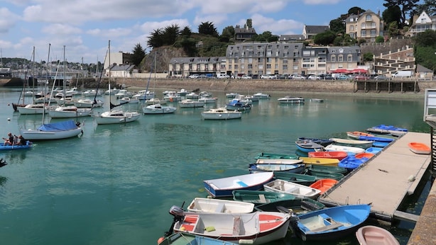 Un port de plaisance où sont amarrés différents types de bateaux, une jetée et des bâtiments en arrière-plan.