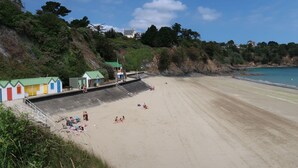 Une plage avec un poste de surveillance pour les sauveteurs, un petit bâtiment aux portes colorées et, en arrière-plan, une colline rocheuse.
