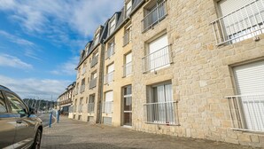 Une rangée de bâtiments en pierre dotés de balcons et de grandes fenêtres, une rue pavée et une voiture garée.