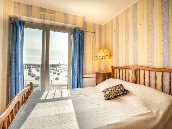 A hotel room with a bed, a nightstand, a lamp, and a view of boats through the window.