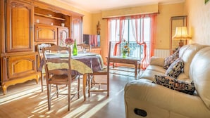 Un coin repas avec une table en bois dressée pour quatre personnes, un canapé agrémenté de coussins à motifs et une fenêtre ornée de rideaux légers.