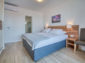 Ein ordentlich eingerichtetes Schlafzimmer mit Bett, Nachttischen, einem Sessel und einem Bild an der Wand.