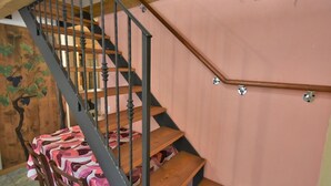 A wooden staircase with a metal railing, a table with a colorful tablecloth, and a wall with a grapevine mural.