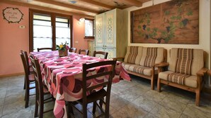 A dining area with a table set for four, wooden chairs, a sofa, and a large painting on the wall.