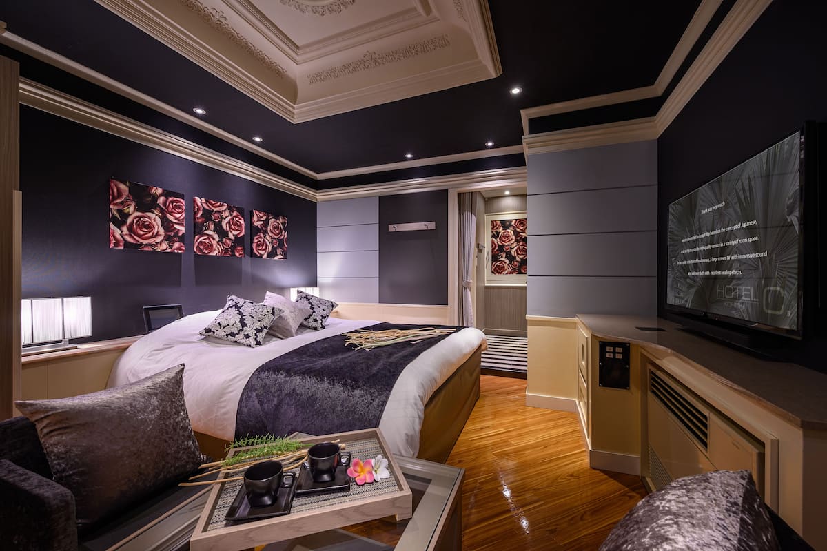 A modern hotel room with a large bed, a TV, and a dining area with a tray of food and drinks.