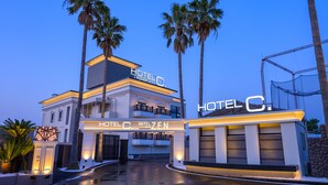 Een moderne hotelentree met een opvallend bord, palmbomen en een goed verlichte oprit.