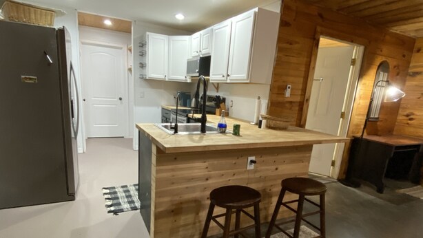 A modern kitchen with a wooden island, white cabinets, and a black refrigerator.