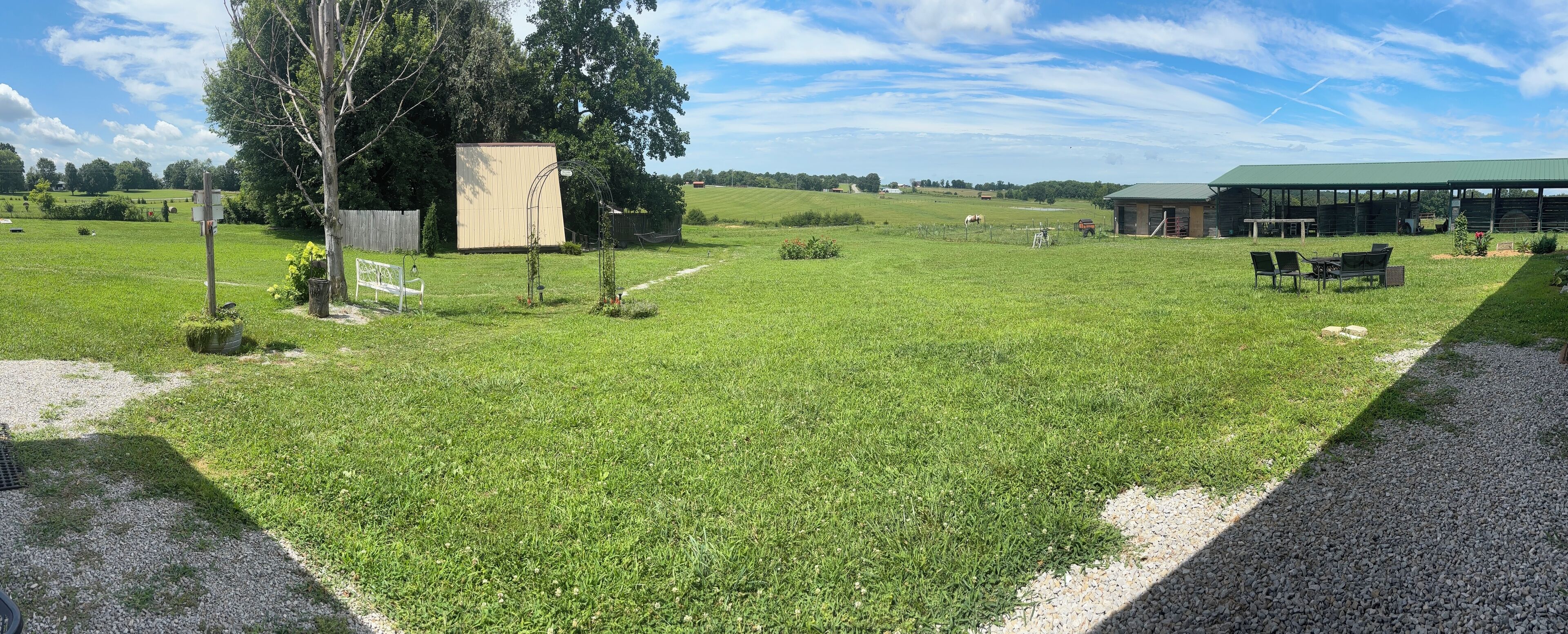 A grassy field with a barn, a fenced area, and a gravel path.