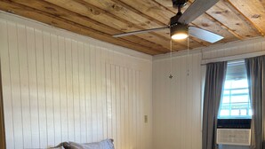 A bedroom with a bed, a ceiling fan, a window with curtains, and a wall-mounted heater.
