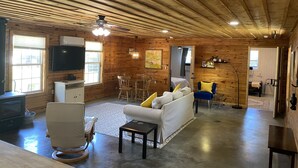 A spacious living area with wooden walls and ceiling, a dining table with chairs, a sofa, a TV, and a ceiling fan.