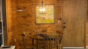 A wooden-paneled room with a dining table and chairs, a painting on the wall, and a door.
