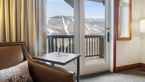 Ein Hotelzimmer mit Balkon, einem Tisch mit zwei Sektgläsern, einem Ledersessel und Blick auf schneebedeckte Berge.