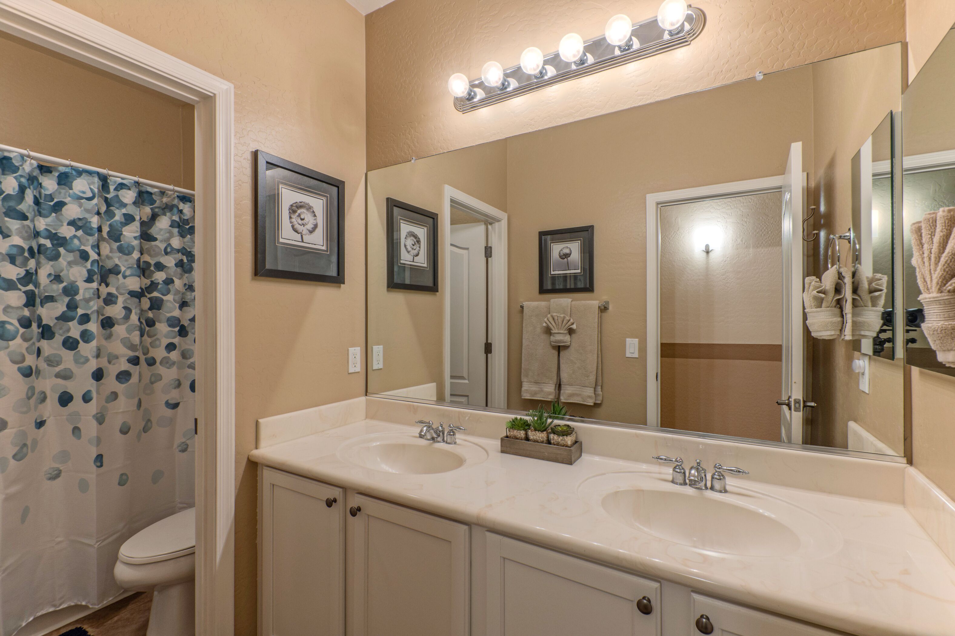 A bathroom with two sinks, a shower, and a large mirror with lights.