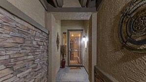 A stone-walled hallway leading to a door with a glass panel, a red vase, and a decorative wall piece. - Resort Amenities: Pvt Htd POOL, Putt Green, Patio & Gas Grill & Fire Tbl, TVs All BRs, (Gilbert)