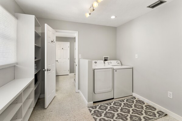 A laundry room with a washing machine and dryer, a patterned rug, and a white door leading to another room.