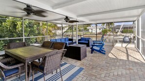 Un patio techado al aire libre con mobiliario de mimbre, ventiladores de techo y vistas del paisaje circundante.
