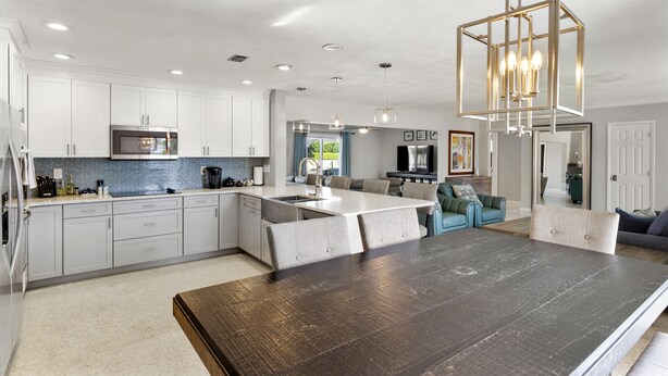 Una cocina moderna con armarios blancos, una isla central y una mesa de comedor de madera oscura.