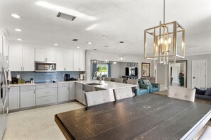 A modern kitchen with white cabinets, a central island, and a dark wooden dining table.